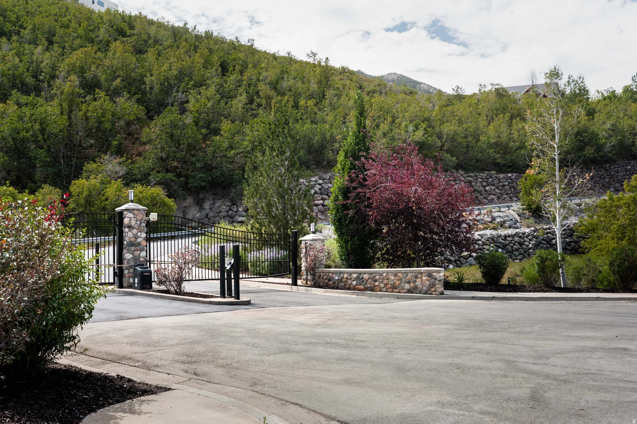 Wrought iron automatic gate with stone pillars, stone retaining walls, and mature landscaping