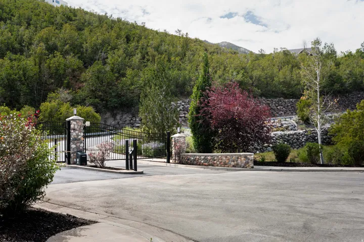 Wrought iron automatic gate with stone pillars, stone retaining walls, and mature landscaping