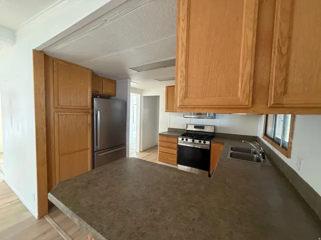 Kitchen with wood-finish cabinetry, stainless steel appliances, a dual basin sink, and a counter with an integrated breakfast bar