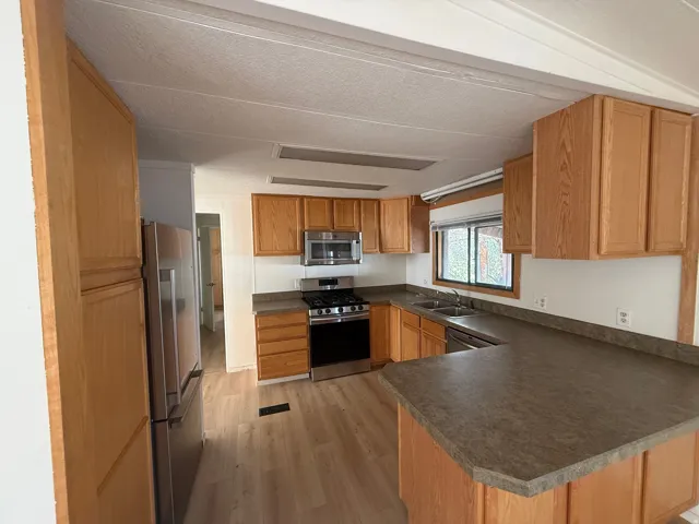 U-shaped kitchen featuring light wood cabinetry, stainless steel appliances, and wood-finish flooring