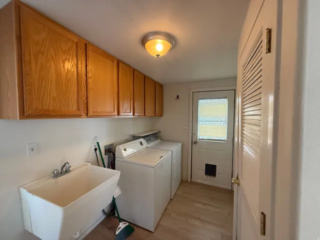 Laundry area featuring wood-finish cabinetry, a utility sink, and a louvered door