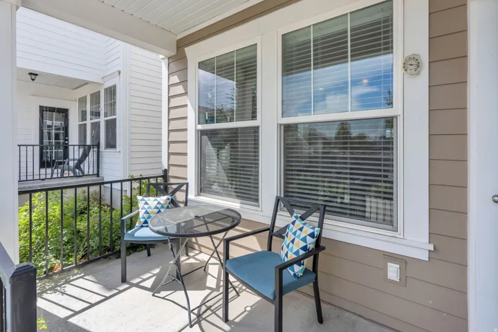 Covered porch with concrete flooring, framed by black metal railings, and featuring a window with blinds