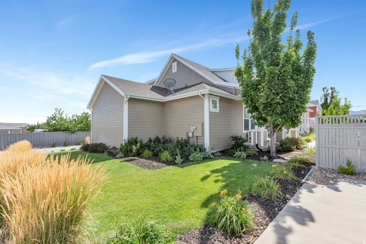 Manicured lawn with mature trees and ornamental grasses, complemented by concrete paving and a privacy fence