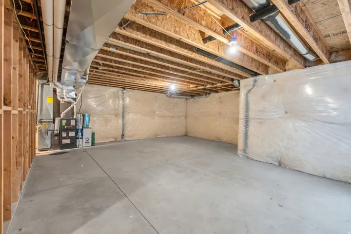 Unfinished basement featuring exposed wood framing, concrete flooring, visible HVAC ductwork, utility systems, and insulated walls