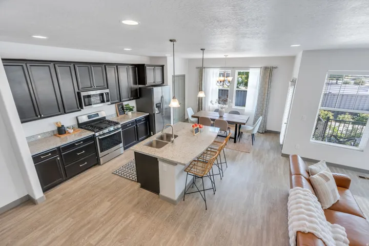 Open-concept living area with wood-finish flooring, a kitchen island with seating, a dining area with a chandelier, and a kitchen featuring dark cabinetry and stainless steel appliances