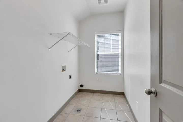 Bright, light-filled hallway featuring tile flooring, white drywall construction, and a large window with plantation shutters providing natural illumination