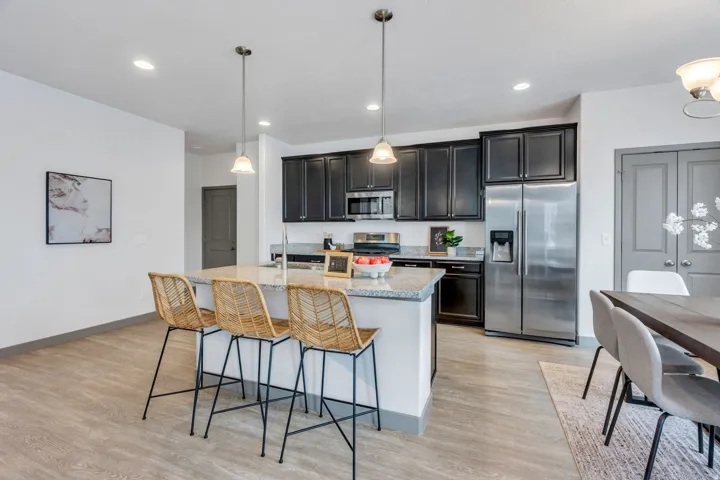 Kitchen featuring dark cabinetry, stainless steel appliances, a large island with a stone countertop, and pendant lighting