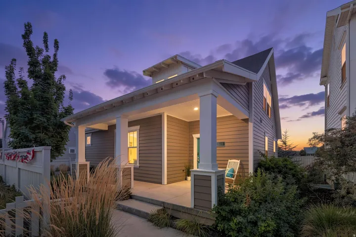 Covered front porch with substantial columns, horizontal siding exterior, gabled roofline, and established landscaping