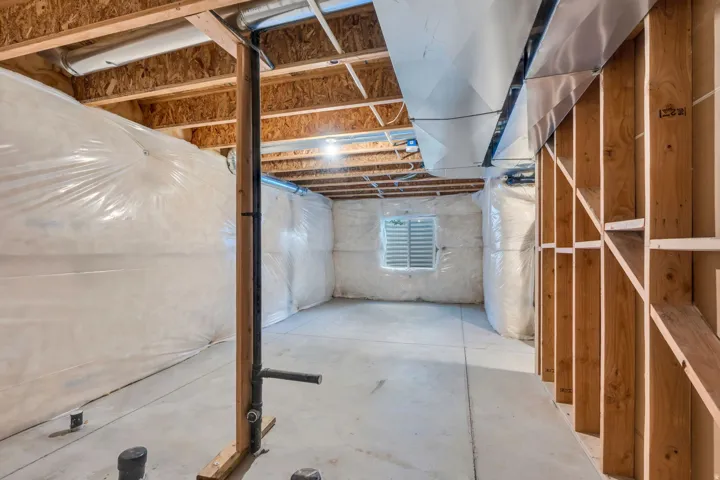 Unfinished basement featuring exposed wood framing, concrete flooring, and an egress window