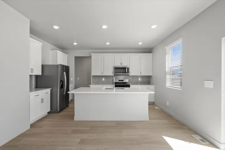 **Disclaimer** Interior package has upgrades not photographed.  Modern kitchen featuring white cabinetry, stainless steel appliances, quartz countertops, a large center island with seating, and recessed ceiling lighting