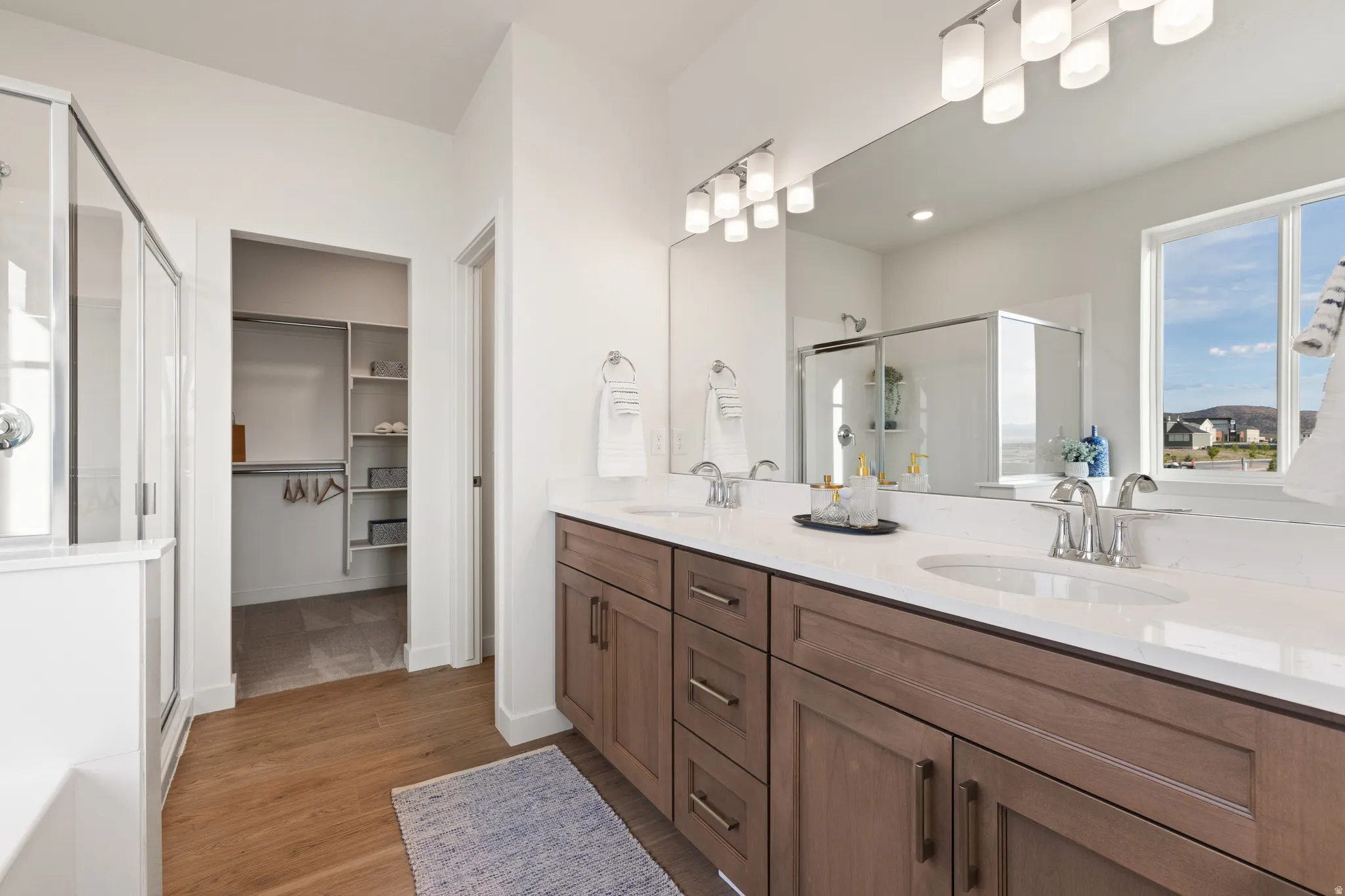 Wood-finish flooring, dual vanity with undermount sinks, frameless glass shower enclosure, and a walk-in closet with built-in shelving