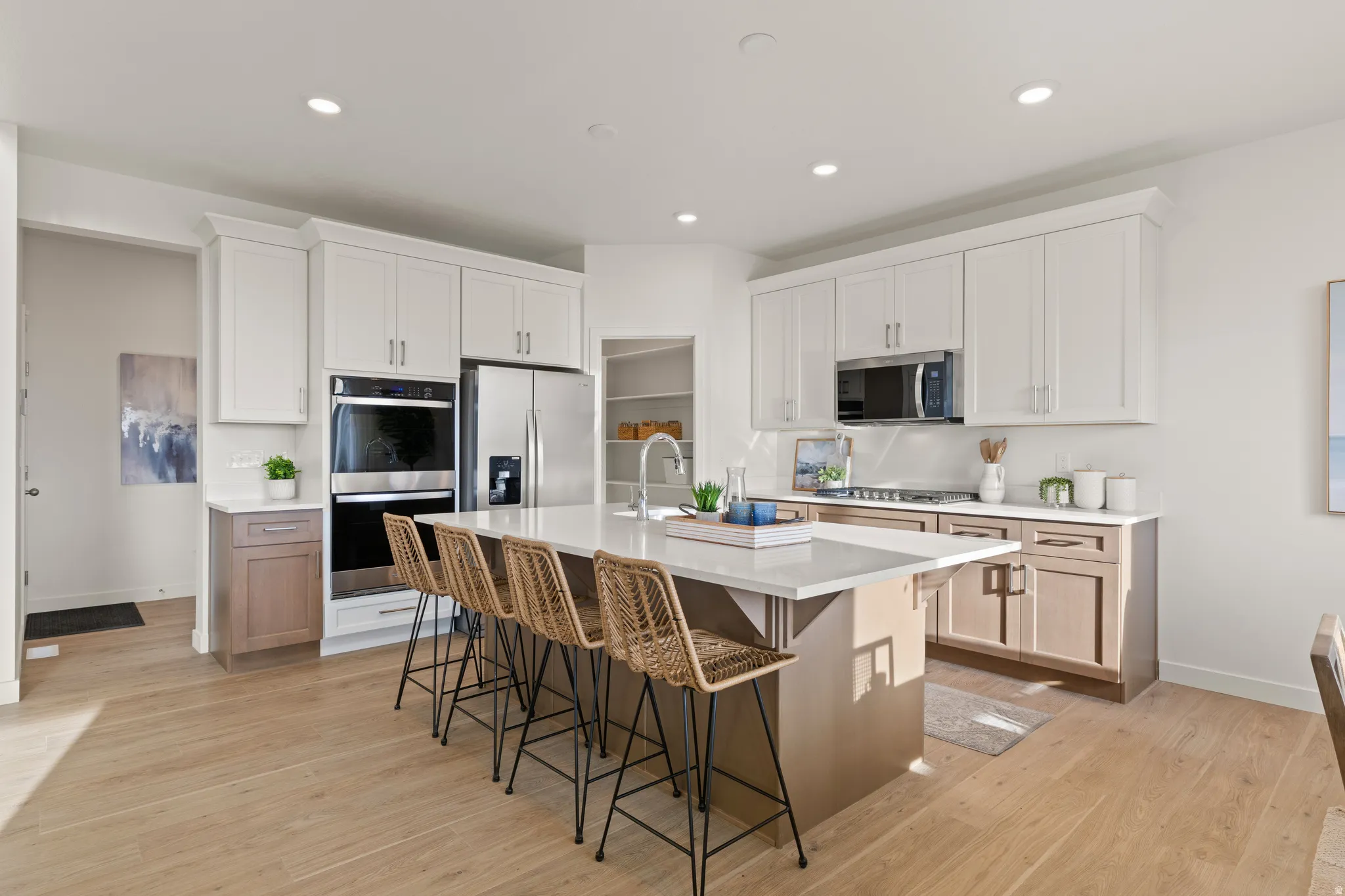 Kitchen with wood-finish flooring, two-tone cabinetry, stainless steel appliances, a center island with countertop seating, and recessed lighting