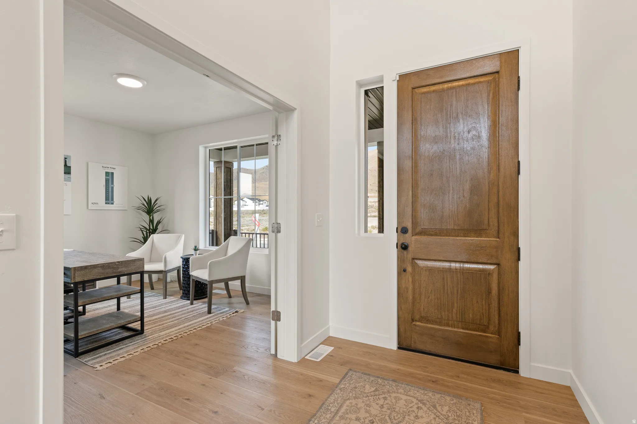 Hardwood flooring, natural wood entry door with black hardware, white trim, recessed lighting, and an open doorway