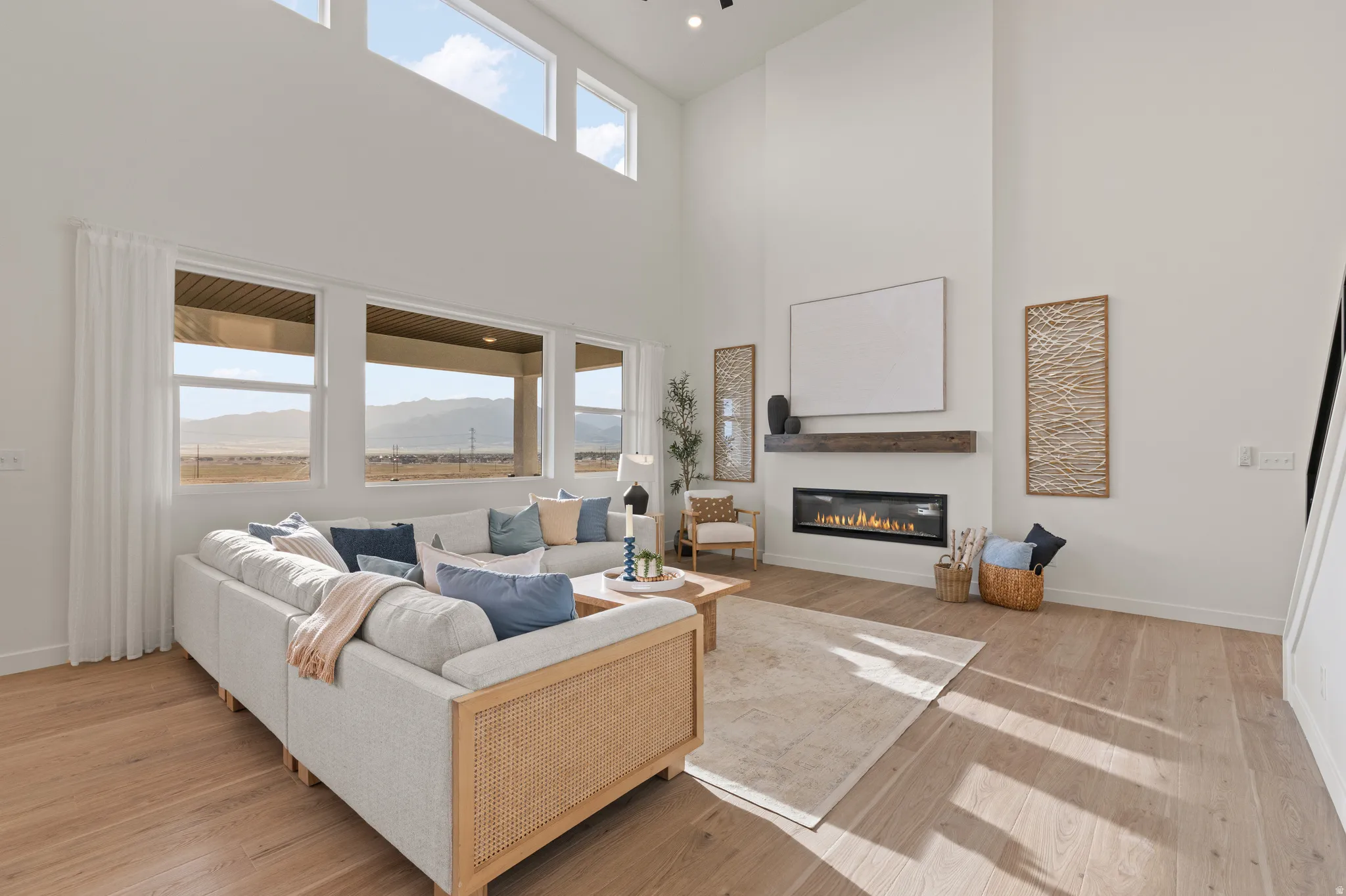 Vaulted ceilings, expansive windows, light wood-finish flooring, and a linear fireplace with a wood mantle