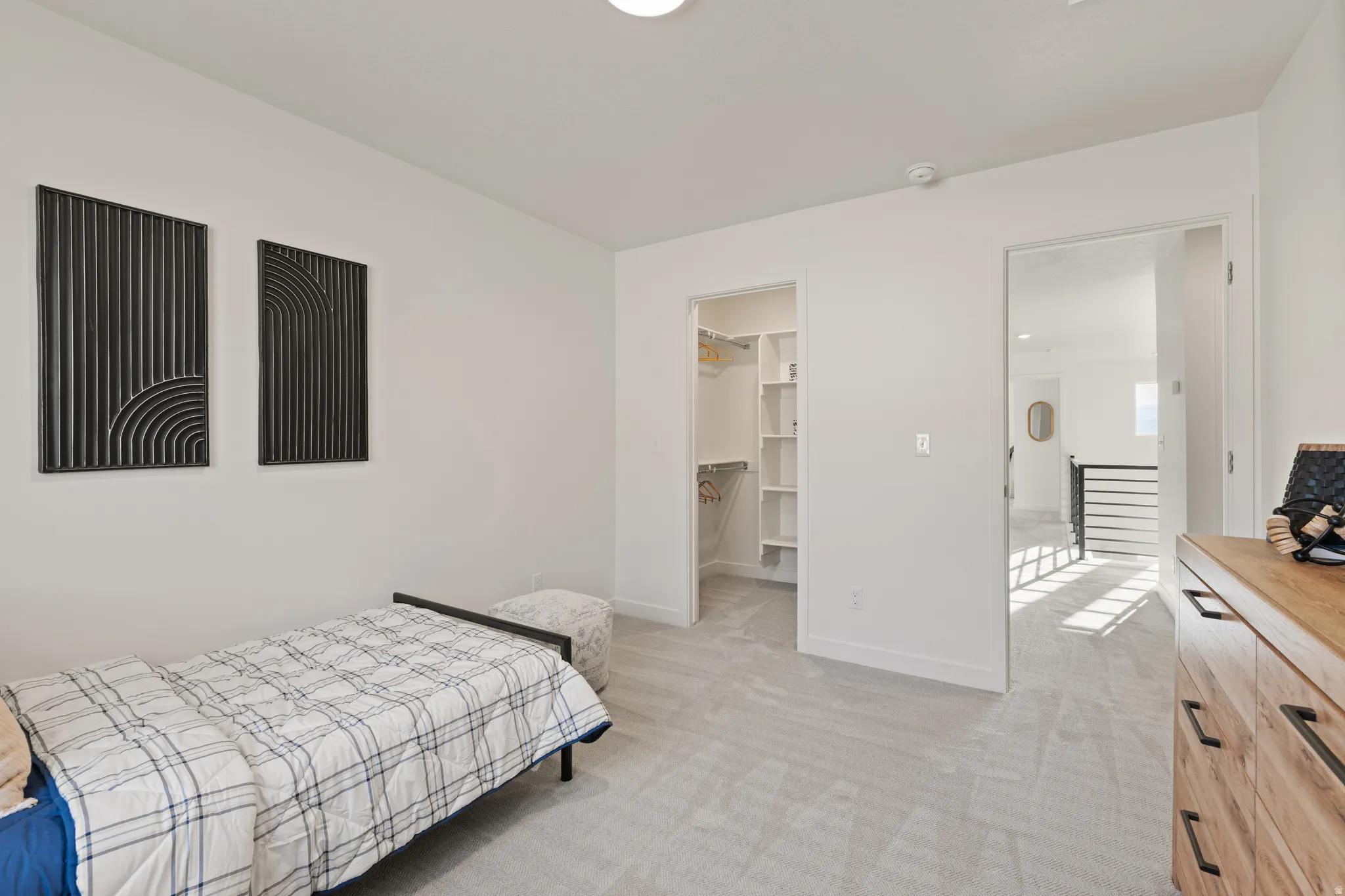 Recessed lighting, light gray carpeting, walk-in closet with built-in shelving, white walls, and a light wood-finish dresser with black hardware