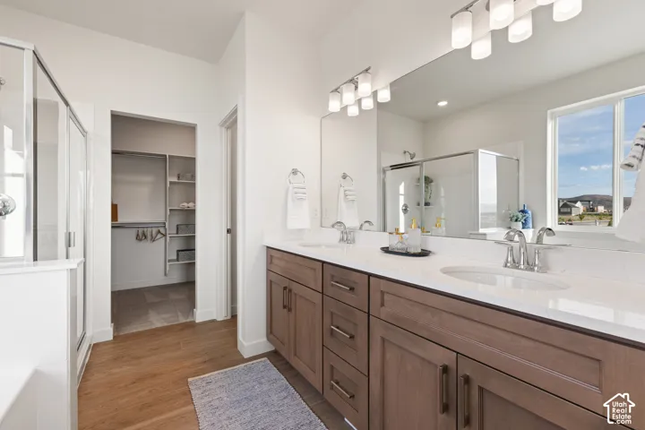 Wood-finish flooring, dual vanity with undermount sinks, frameless glass shower enclosure, and a walk-in closet with built-in shelving