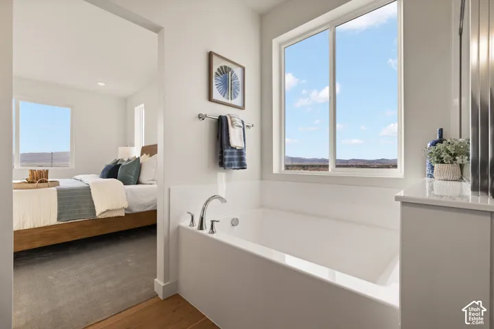Built-in soaking tub with chrome fixtures, large window, and light-toned vanity with a solid surface countertop