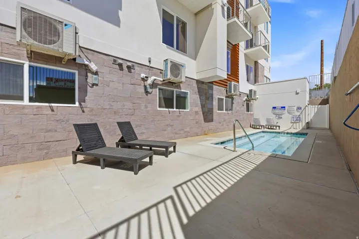 Compact outdoor pool area with integrated spa, concrete decking, and stone-clad exterior wall