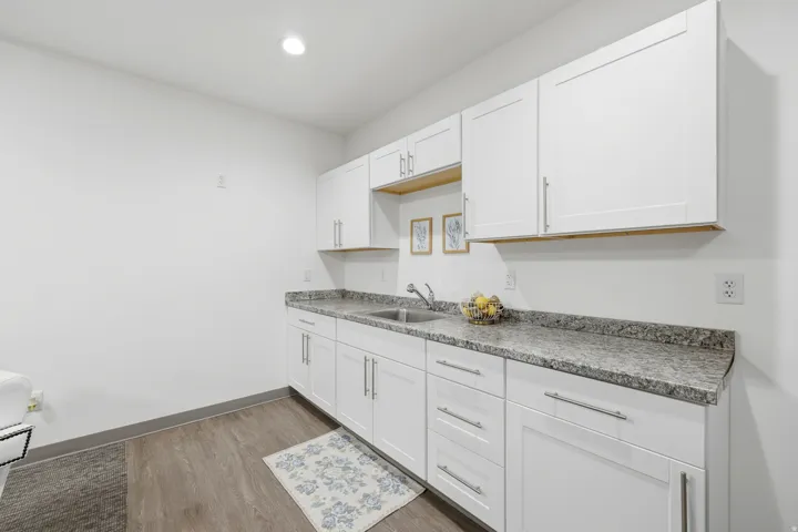 White shaker-style cabinetry with satin nickel hardware, a stainless steel sink, a gray granite-style countertop, and wood-finish flooring