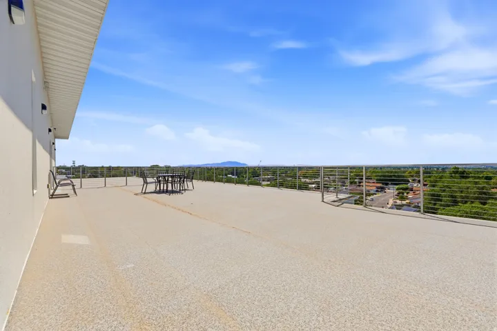Expansive outdoor terrace featuring a textured concrete surface, cable railing, and multiple wall-mounted exterior light fixtures