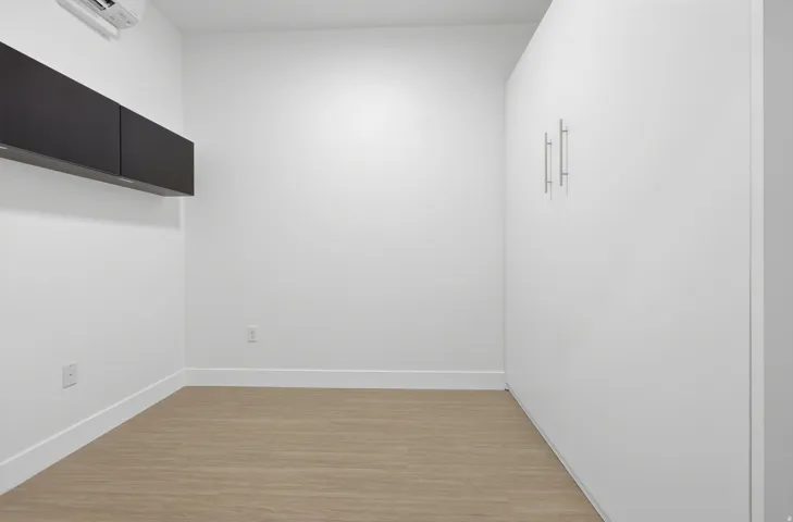 Wood-finish flooring, white walls, and built-in white cabinetry with chrome hardware