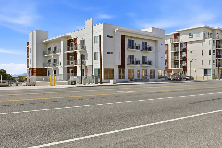 Contemporary multi-story building featuring white facade, wood-tone panel accents, multiple private balconies with black railings, and ground-level windows