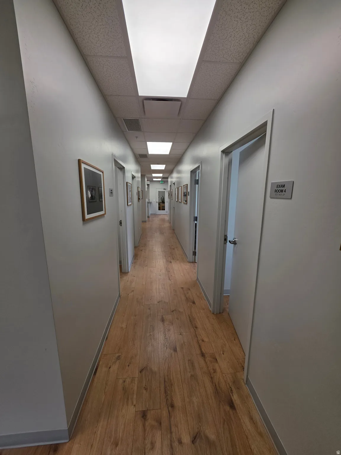 Long hallway featuring wood-finish flooring, white walls, and recessed lighting