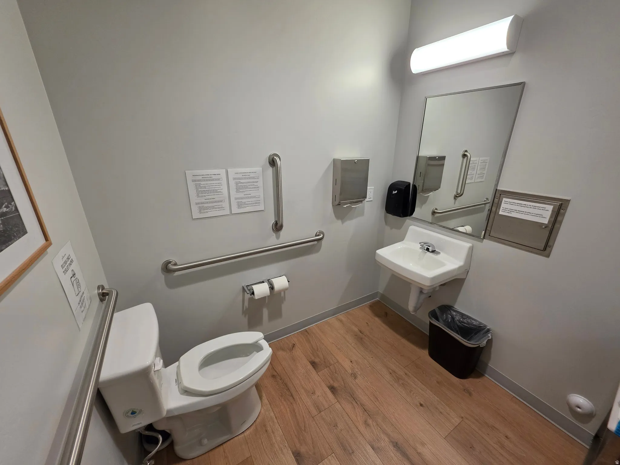Wood-finish flooring, wall-mounted sink, rectangular mirror, and ceiling-mounted linear light fixture