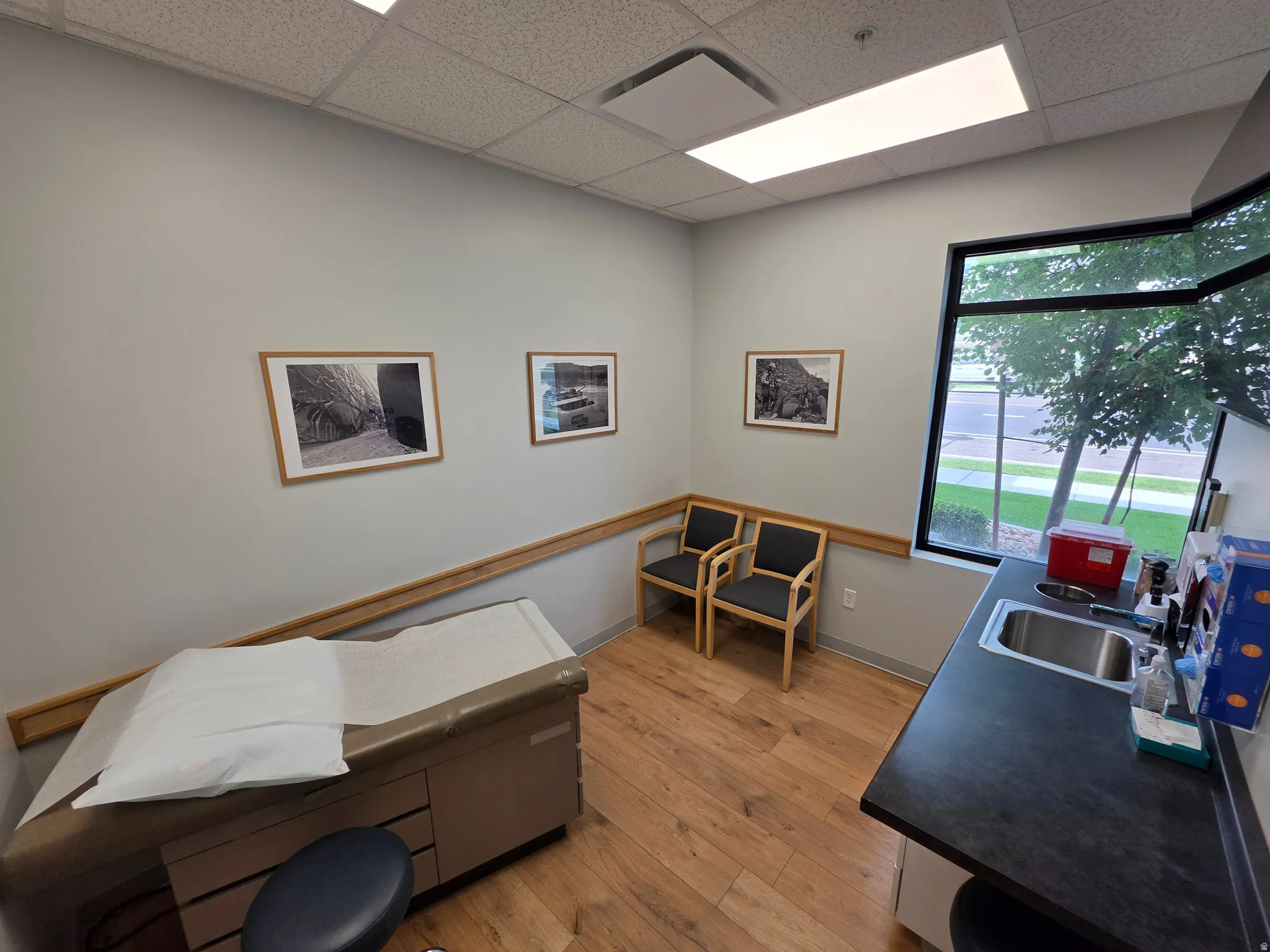 Wood-finish flooring, built-in counter with stainless steel sink, large window, and suspended ceiling with recessed lighting