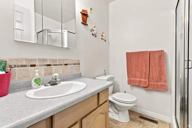 Bathroom featuring a vanity with a built-in sink, cabinet storage, a tiled backsplash, a wall-mounted medicine cabinet, and a shower enclosure