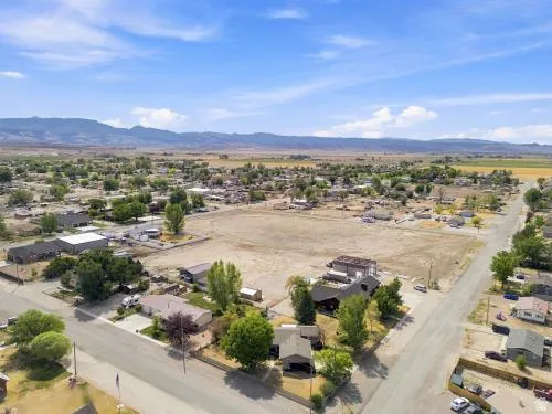 Expansive land parcel with surrounding residential properties, paved road access, and distant mountain backdrop