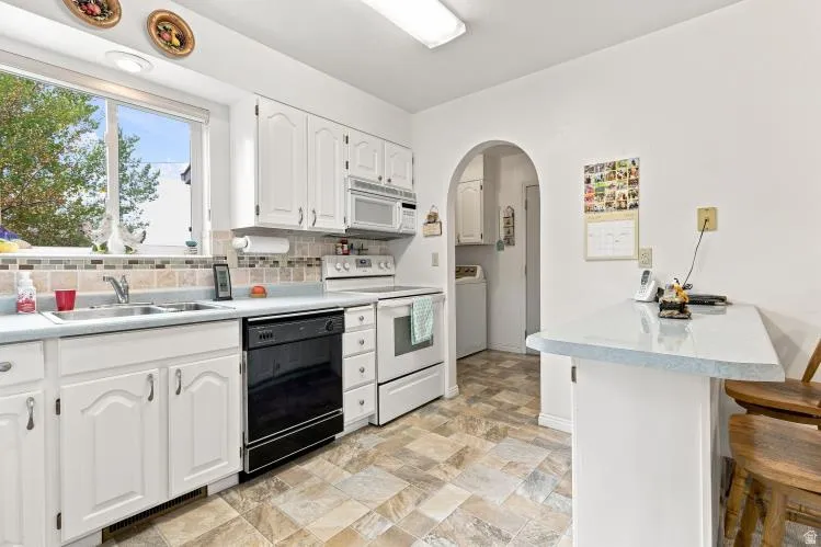 Kitchen featuring white cabinetry, light-toned countertops, a black built-in dishwasher, and an arched doorway