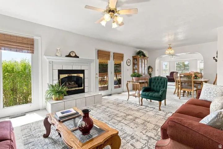 Living room featuring a fireplace with a tile hearth and mantel, ceiling fan, and access to an outdoor area through a glass door