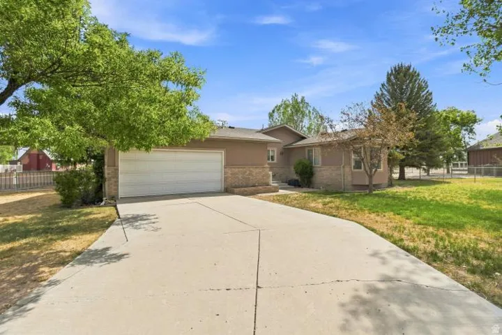 Concrete driveway, attached two-car garage, stucco exterior with stone accents, mature landscaping, and a fenced yard