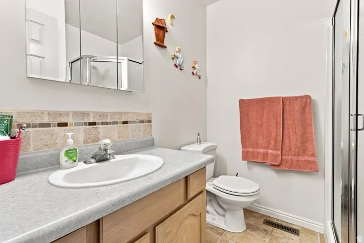 Bathroom featuring a vanity with a built-in sink, cabinet storage, a tiled backsplash, a wall-mounted medicine cabinet, and a shower enclosure