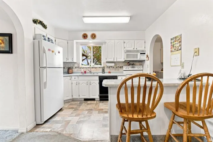 White cabinetry, tiled flooring, white appliances, and a built-in breakfast bar