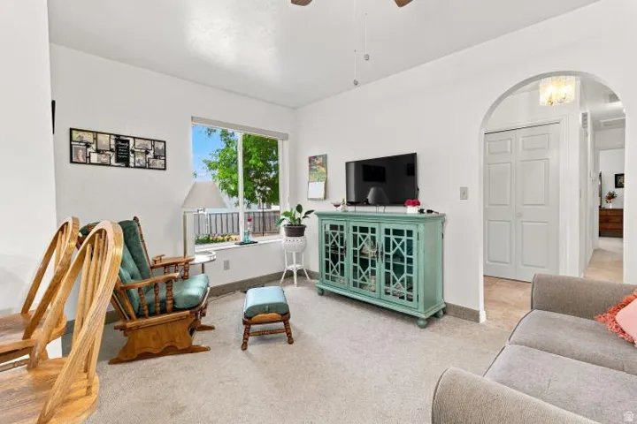 Carpeted living area featuring a large window, a ceiling fan, and an arched doorway