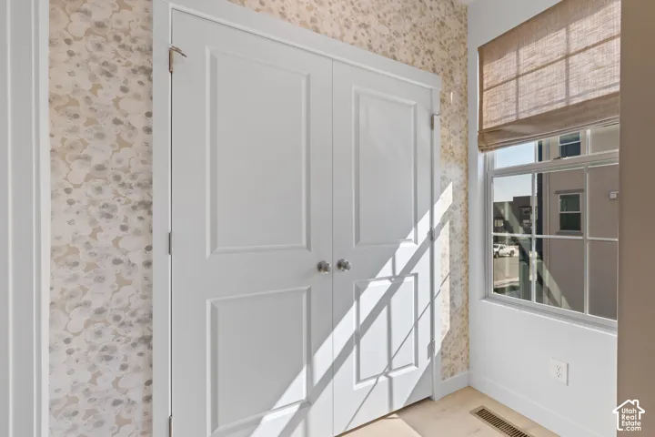 Double panel doors, patterned wallcovering, large window, woven Roman shade, and light wood-finish flooring