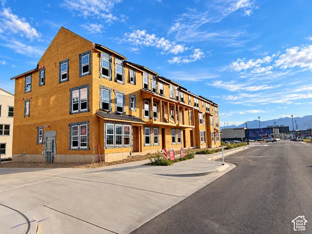 New construction multi-level building with multiple window units, concrete sidewalk, and paved street
