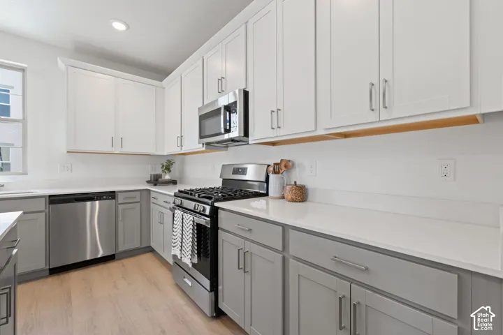 Kitchen featuring light wood-finish flooring, two-tone cabinetry with white upper and grey lower units, stainless steel gas range, stainless steel microwave, and stainless steel dishwasher