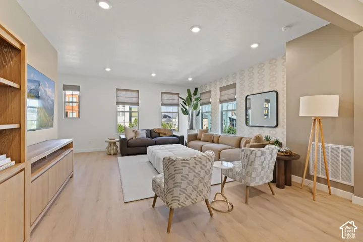 Recessed lighting, light wood-finish flooring, built-in shelving, multiple windows, and accent wall with patterned wallpaper