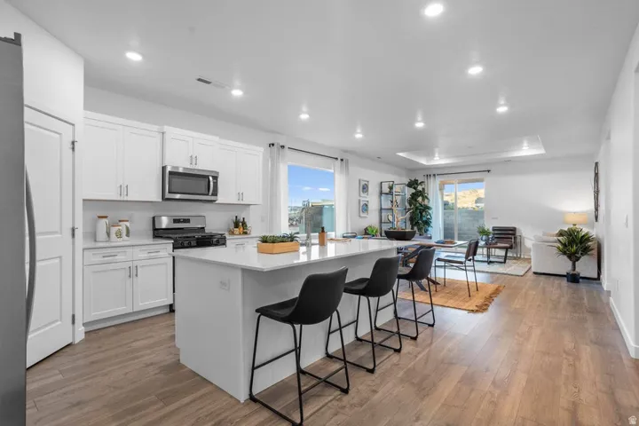 Modern kitchen featuring white shaker cabinets, stainless steel appliances, a large center island, and wood-finish flooring