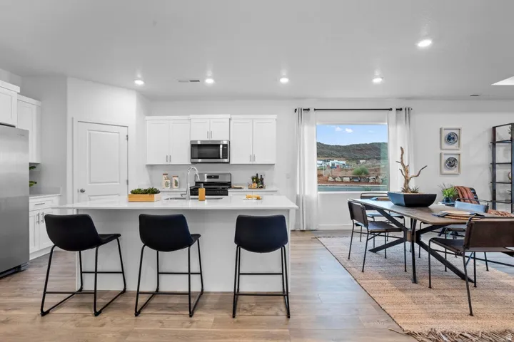 Open-concept kitchen and dining area featuring white cabinetry, stainless steel appliances, a center island with seating, wood-finish flooring, and a large window
