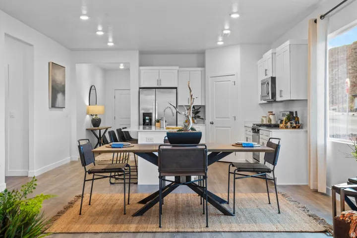 Open-concept living space with recessed lighting, wood-finish flooring, white cabinetry, stainless steel appliances, and a kitchen island with a basin sink