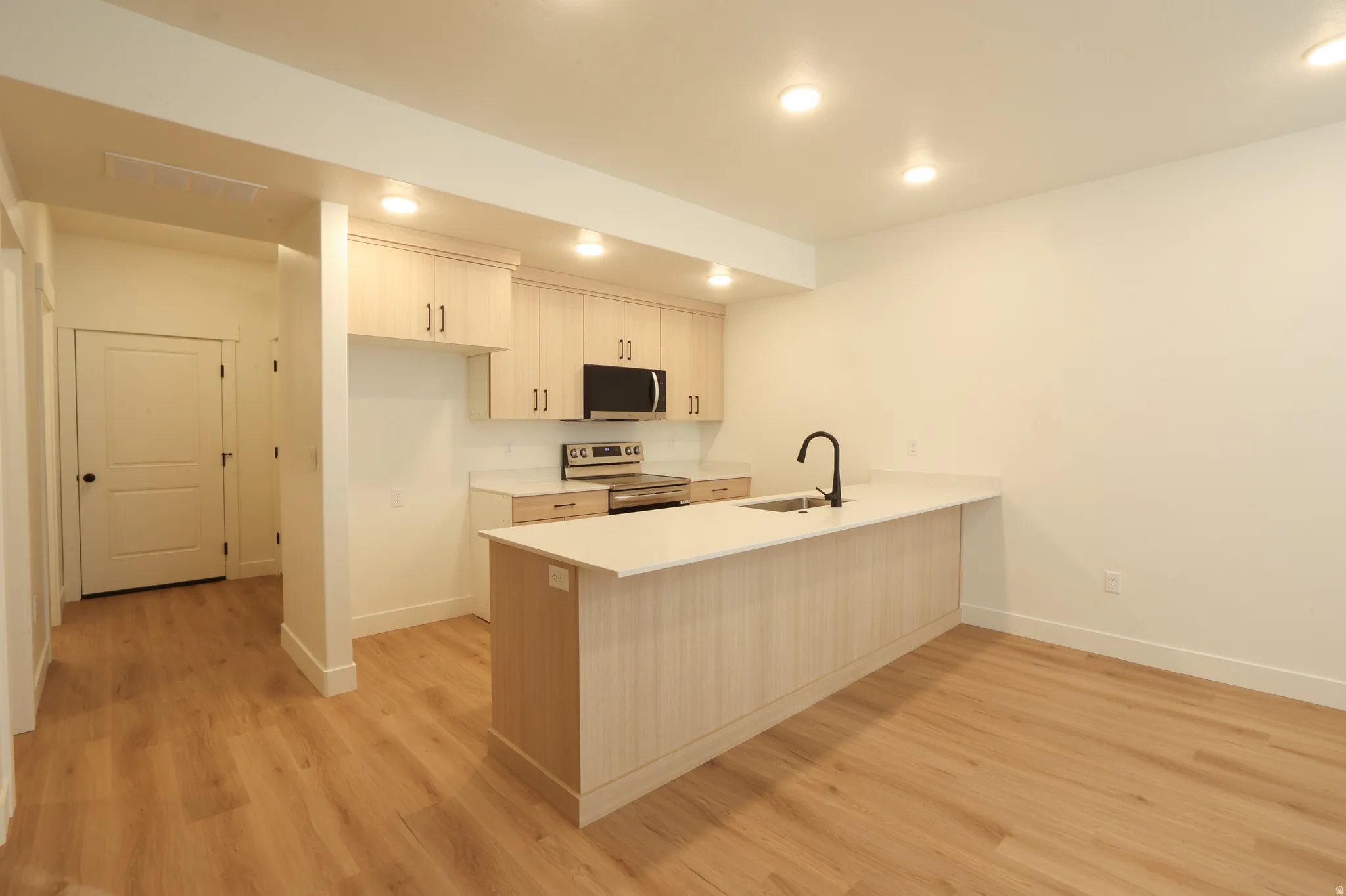 Kitchen featuring wood-finish flooring, recessed lighting, light-toned cabinetry, light countertops, and a central island with a sink