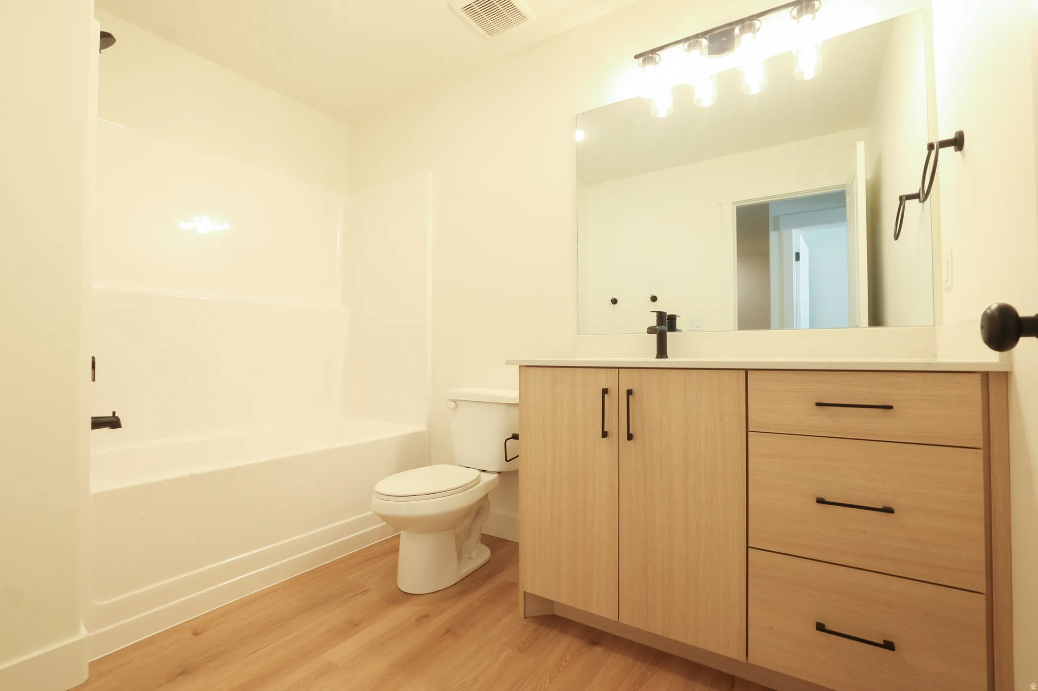 Light wood-finish flooring with a white bathtub and shower surround
