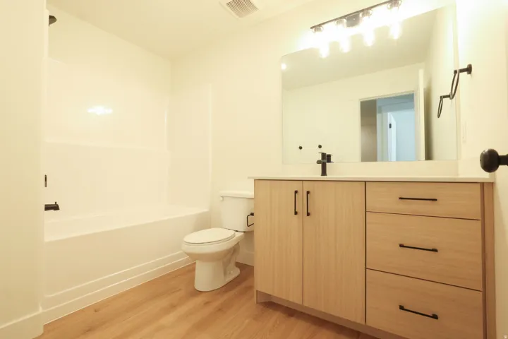 Light wood-finish flooring with a white bathtub and shower surround