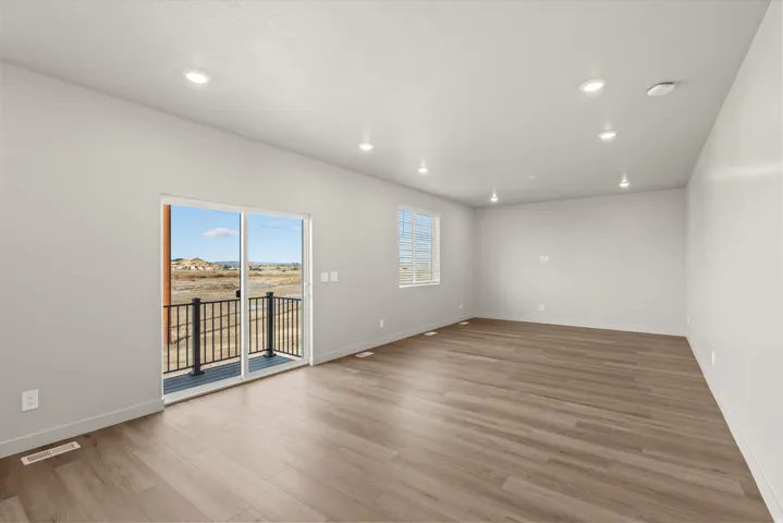 **DISCLAIMER**   Interior package upgrades not photographed. Recessed ceiling lighting, wood-finish flooring, sliding glass door to a balcony, balcony with black metal railing, and a window providing natural light