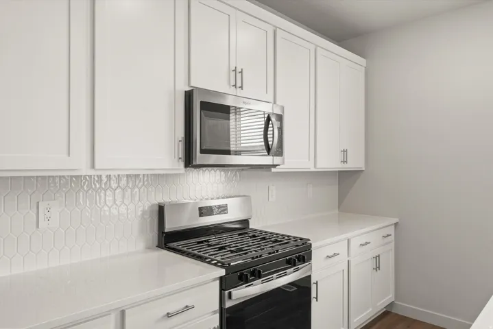 **DISCLAIMER**   Interior package upgrades not photographed. White shaker-style cabinetry, stainless steel microwave, gas range, light-toned countertops, and unique geometric tile backsplash