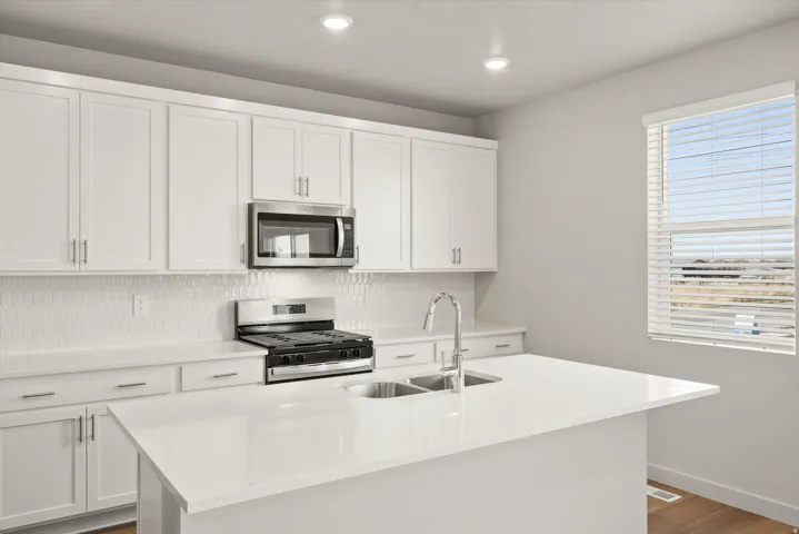 **DISCLAIMER**   Interior package upgrades not photographed. Kitchen featuring white cabinetry, stainless steel appliances, white countertops, a white hexagonal tile backsplash, and wood-finish flooring
